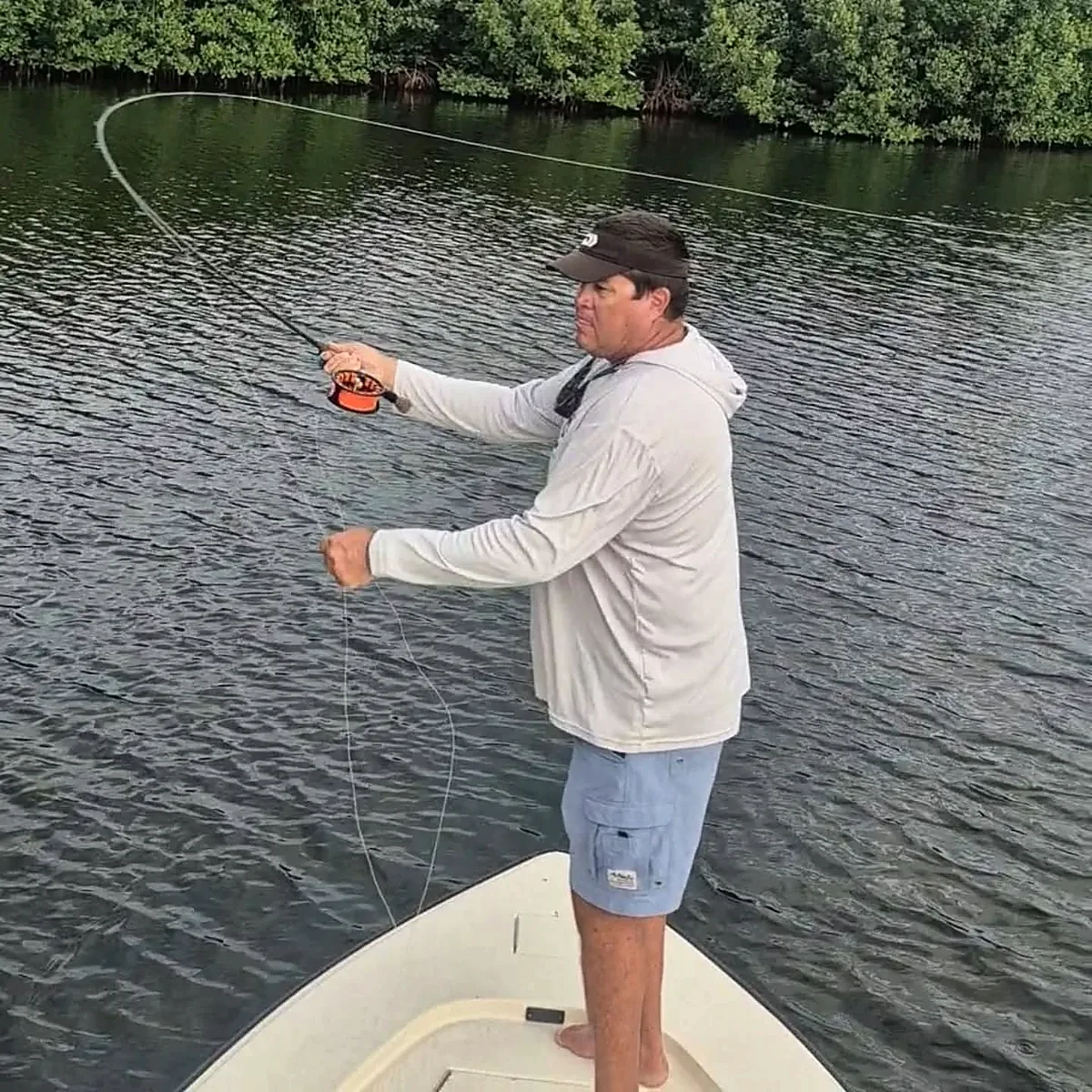 Fly angler casting from the bow of a skiff beside Puerto Rico mangroves.