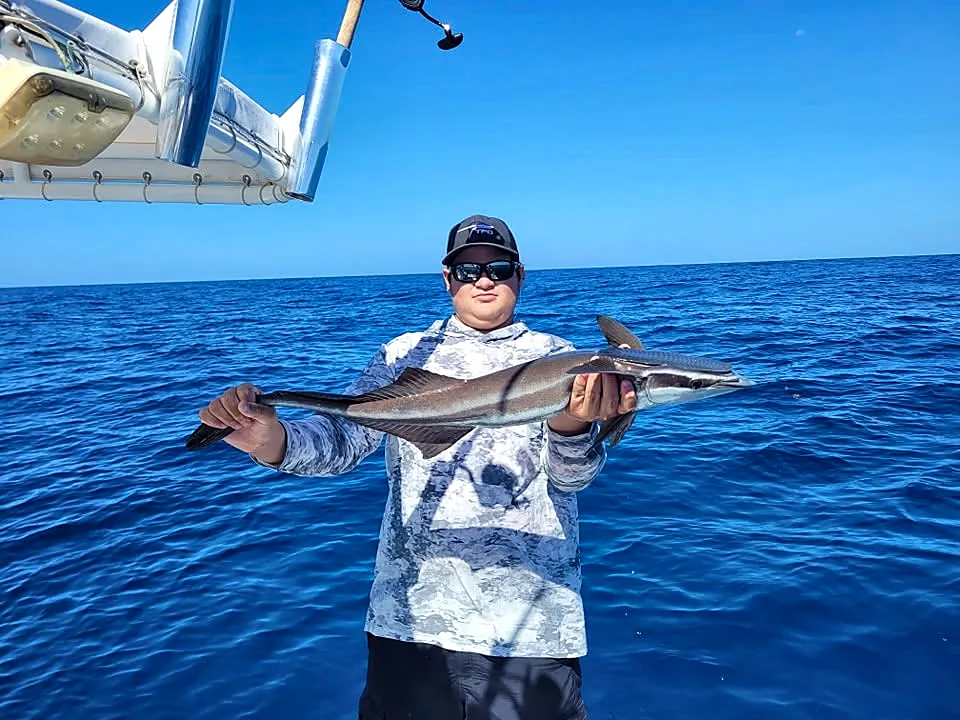 Young angler holding a long offshore fish over deep blue water.
