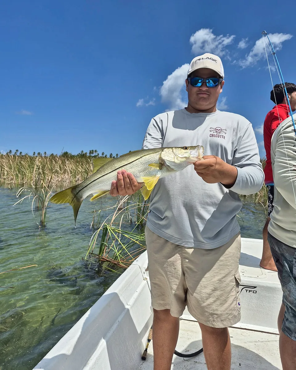 Young angler holding an inshore catch among shallow coastal grasses.