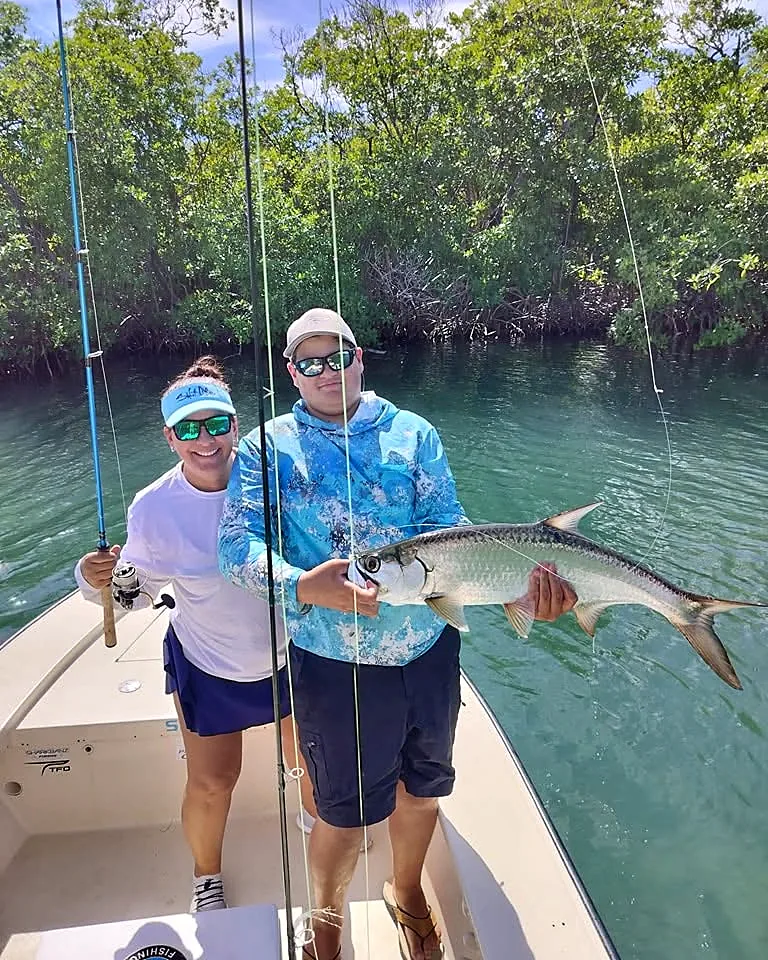 Two guests smiling with a tarpon aboard a shallow-water skiff in Puerto Rico.