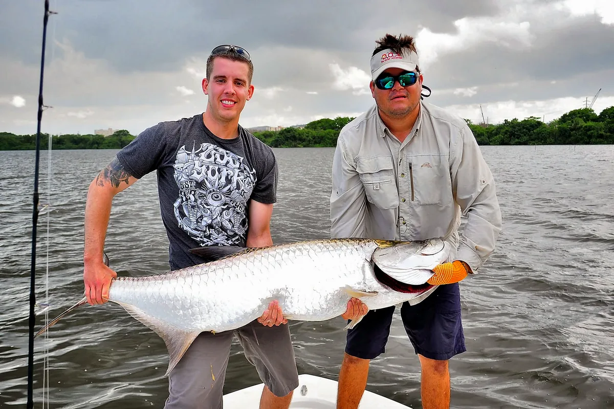 Two anglers holding a large tarpon during a Puerto Rico fishing trip.