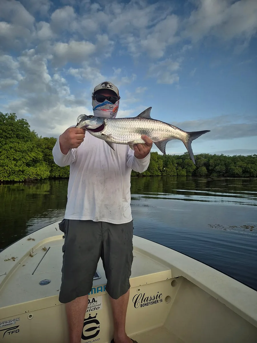 Angler holding a tarpon with calm mangrove water in the background.